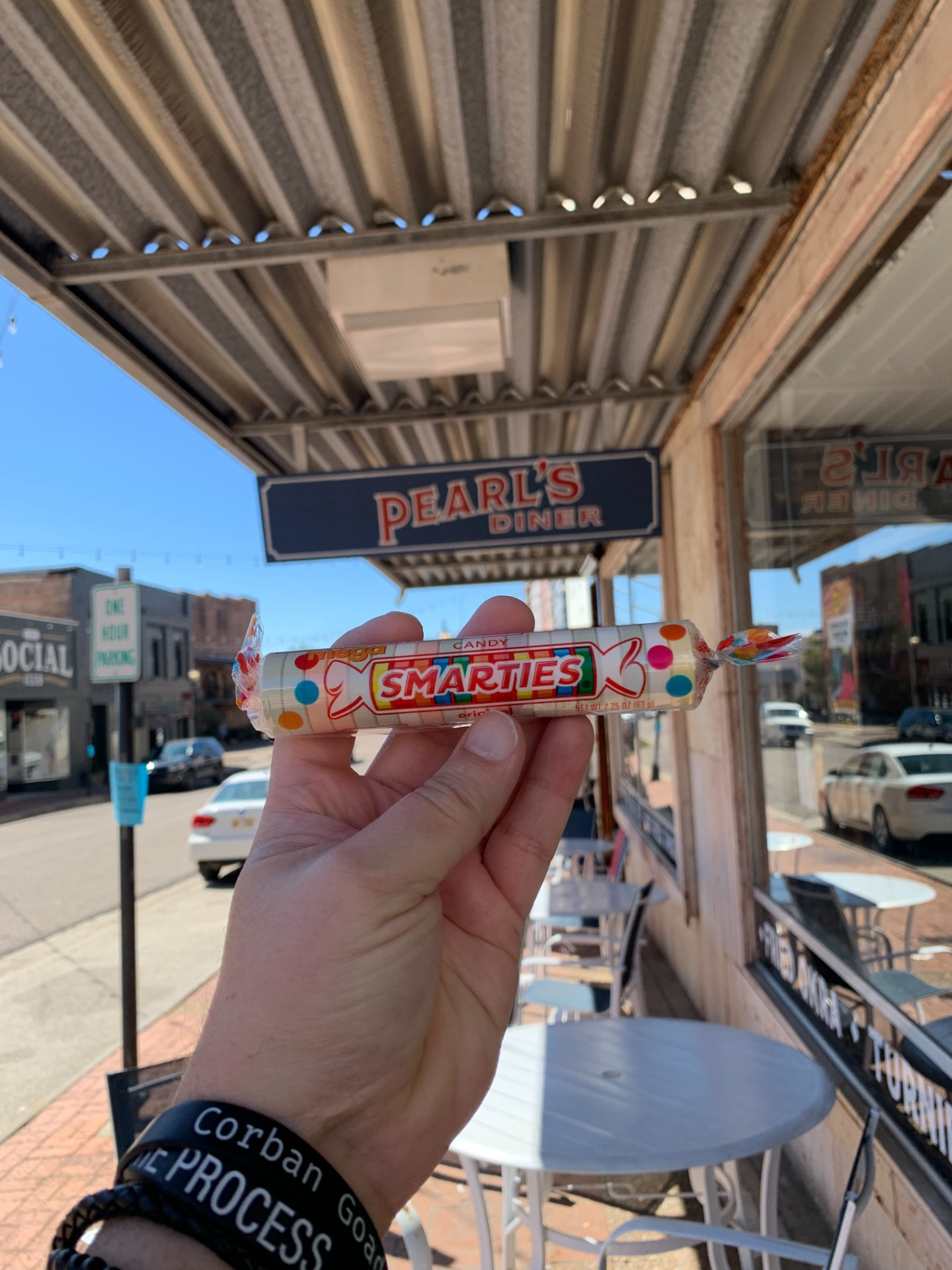 Chester's outstretched hand holds a roll of Smarties in front of the entrance to Pearl's Diner