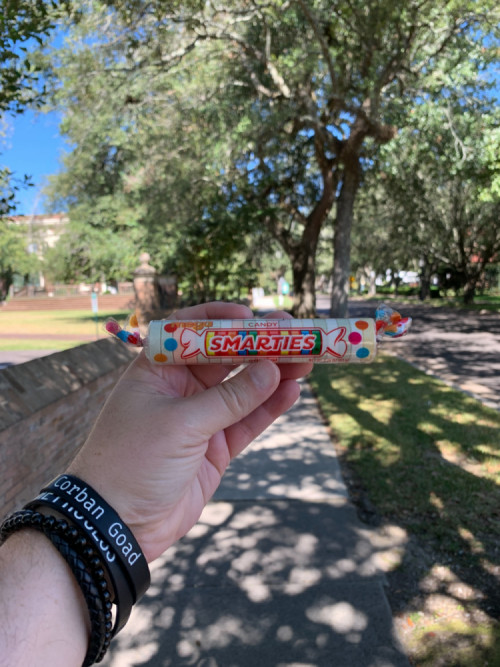 Chester's outstretched hand holding a large Smarties candy roll on the streets of Laurel.