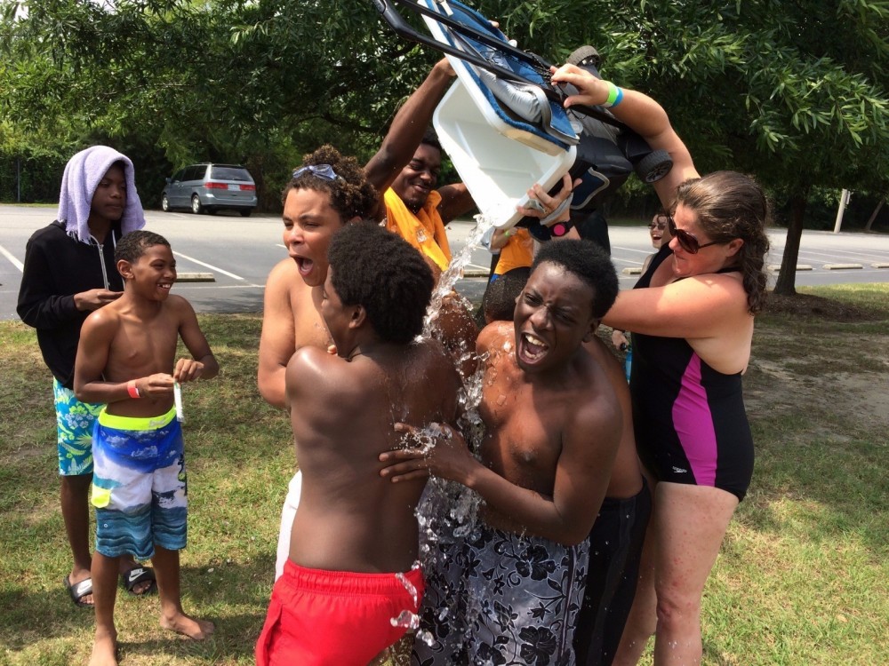 Adult pours water on teens for summer pool party